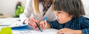 Young boy drawing with psychologist beside him