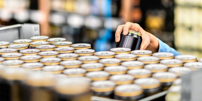 Hand taking beer can from top shelf in supermarket.
